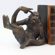 A bronze-finished figurine of a seated primate holding a book between its legs, styled as a bookend next to a vintage-style book on a white background.