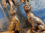 Close-up of two antique gold leopard candlestick holders against blue botanical wallpaper