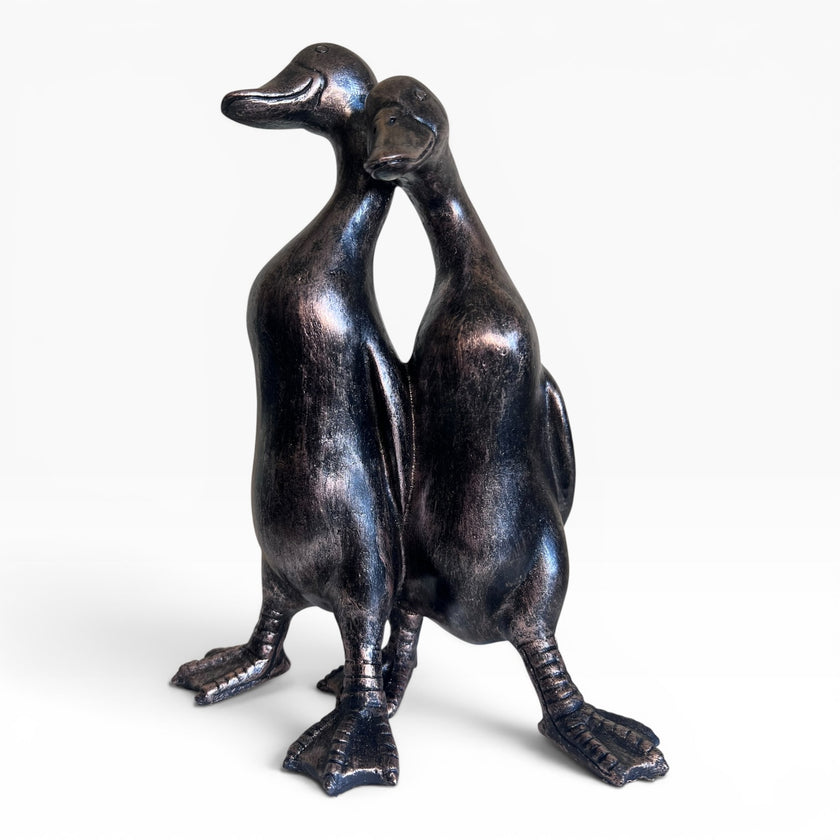 Bronze sculpture of two ducks standing close together on a white background