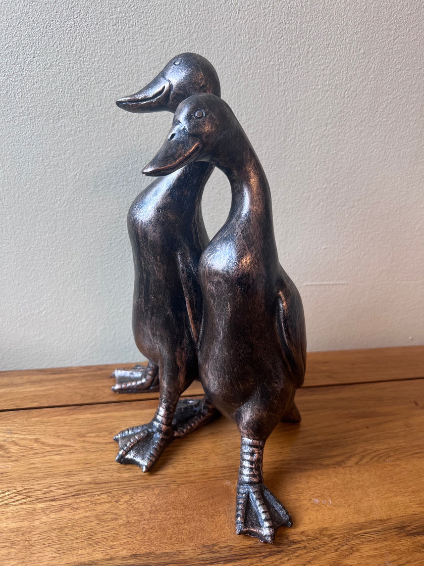 Bronze sculpture of two ducks on a wooden surface
