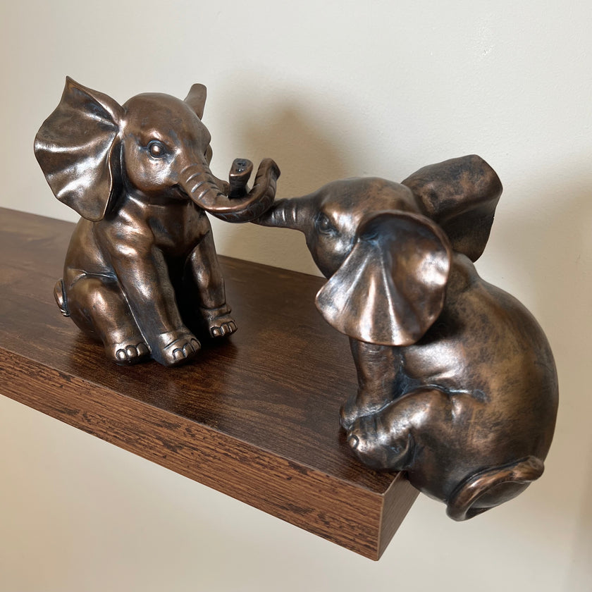 Two antique bronze-effect elephant figurines displayed together on a dark wooden shelf