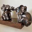 Helping Elephants bronze ornament set displayed across the edge of a dark wooden shelf